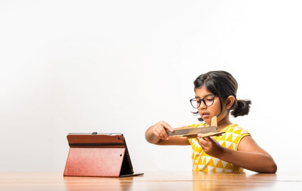 indian small girl student making measuring wings paper plane aeroplane doing school project learning science with online tutorial 3